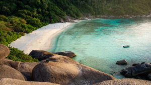 Playa de arena blanca rodeada de vegetación tropical y aguas turquesas en las Islas Similan, Tailandia, vista desde las rocas de granito, con pocos visitantes y una pequeña embarcación en la bahía
