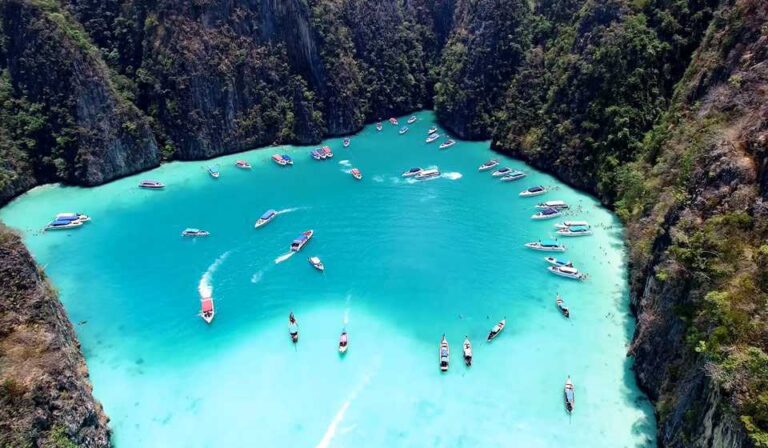 Playa de arena blanca con aguas cristalinas en las Islas Phi Phi, Tailandia, rodeada de acantilados y vegetación tropical.