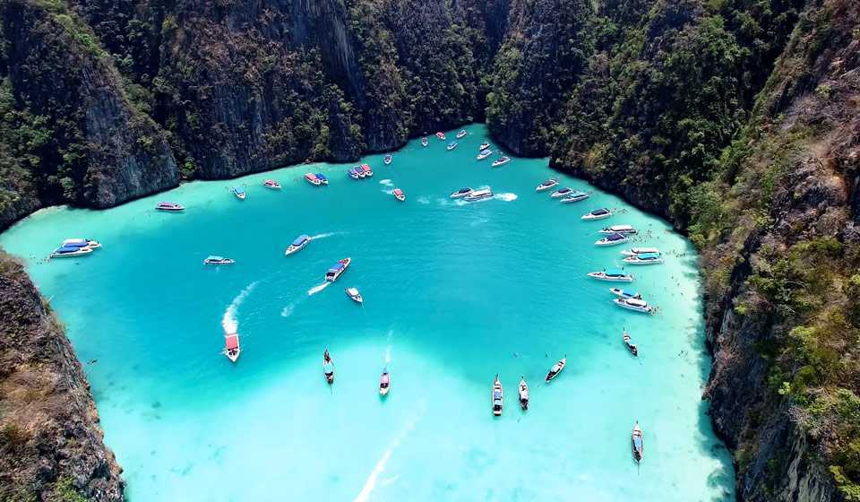 Playa de arena blanca con aguas cristalinas en las Islas Phi Phi, Tailandia, rodeada de acantilados y vegetación tropical.