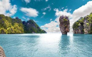 Formación rocosa vertical en medio del mar en la Bahía de Phang Nga, rodeada de acantilados verdes bajo un cielo azul en Tailandia.