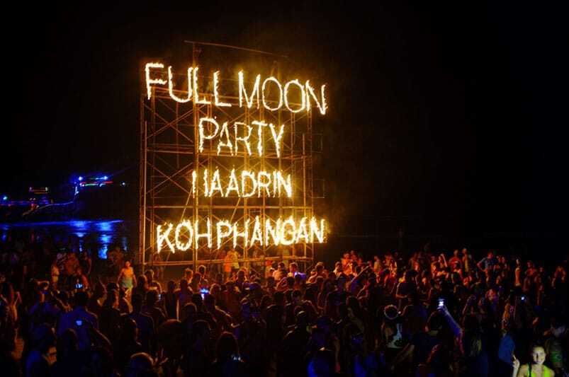 Fiesta nocturna en la playa de Koh Phangan durante la Full Moon Party en Tailandia, con luces, música y bailarines.