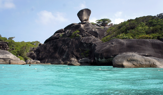 Vista de la célebre formación rocosa de las Islas Similan en Tailandia, donde grandes bloques de granito sobresalen junto al mar turquesa, rodeados de vegetación tropical y cielo despejado.